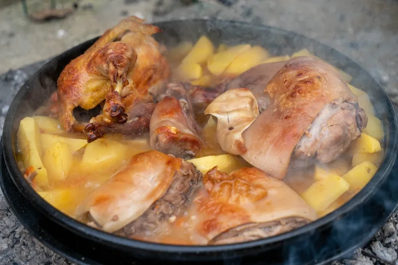Ein fertig geschmortes Gericht wird in der Schmorpfanne auf einem gedeckten Esstisch serviert, umgeben von frischen Kräutern.