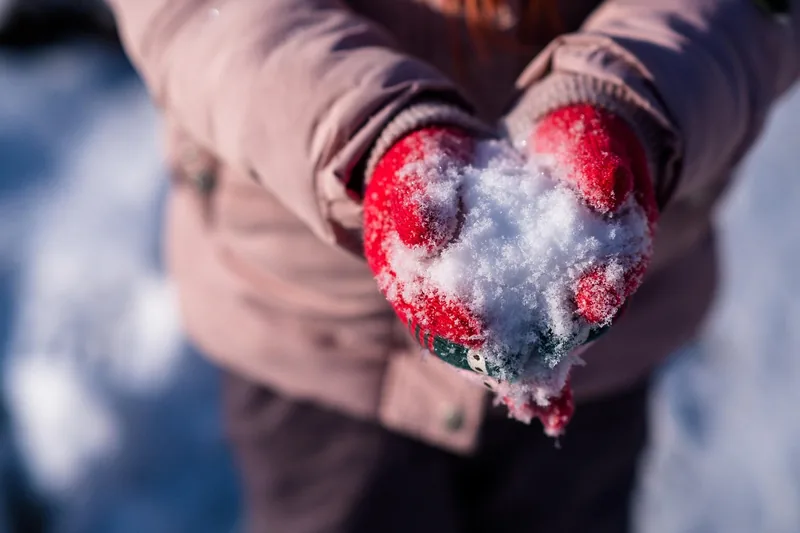 Ein Kind formt mit einem Kinder Schneehandschuh einen Schneeball, Hände gut sichtbar.