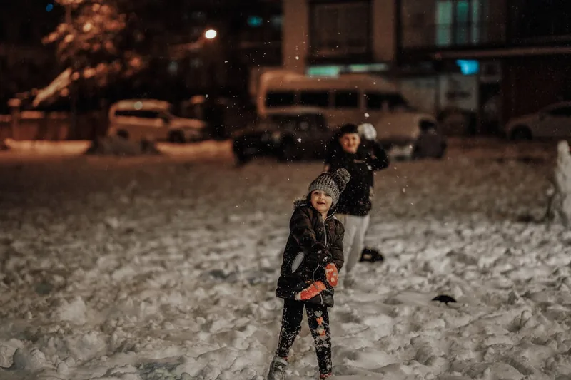 Fröhliche Kinder spielen ausgelassen in einer verschneiten Winterlandschaft, warm eingepackt mit Schneehosen.