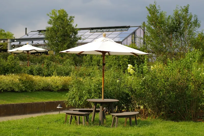 Eine idyllische Gartenlandschaft mit gemütlicher Sitzgruppe im angenehmen Schatten eines Sonnenschirms.