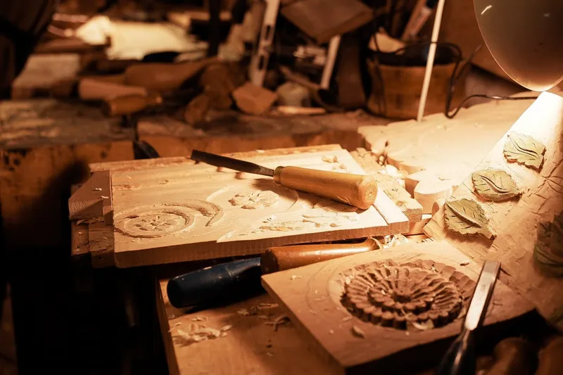 Eine gemütliche Werkstatt-Szene mit fertig geschnitzten Holzfiguren, Werkzeug und Holzspänen auf dem Tisch.
