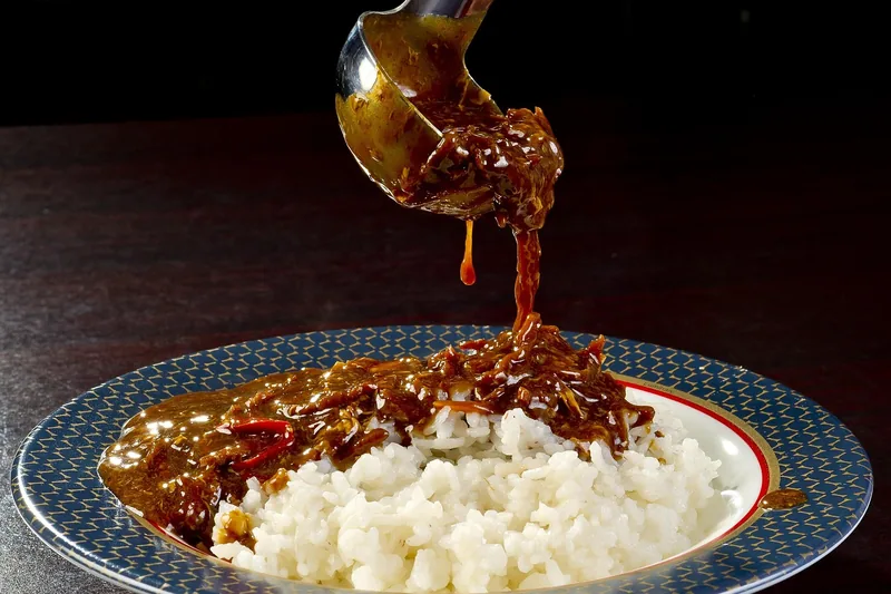 Eine Hand schöpft mit einem Schöpflöffel appetitliche Suppe aus einem Topf in eine Schale.