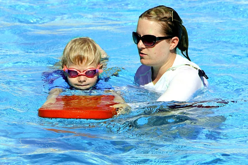 Ein kleines Kind trägt Schwimmflügel und lernt im flachen Wasser zu planschen.