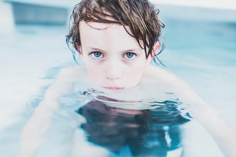 Sonnige Poollandschaft mit spielenden Kindern und Badesachen, die Schwimmflügel andeutet.