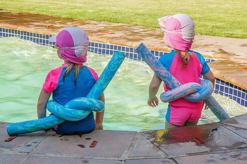 Fröhliche Kinder genießen das Spielen im sonnigen Schwimmbad, symbolisch für sicheres Schwimmen.