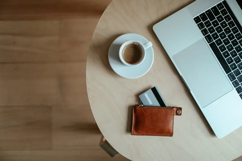 Minimalistischer Arbeitsplatz mit Laptop, Kaffee und einem schlanken Wallet, das modernes Leben symbolisiert.