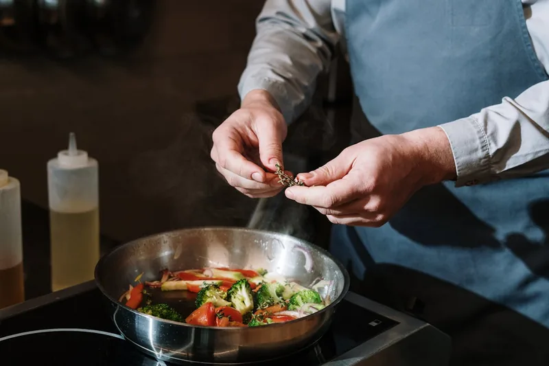 Eine Hand schwenkt eine Servierpfanne mit Gemüse und Fleisch auf einem Herd in der Küche.