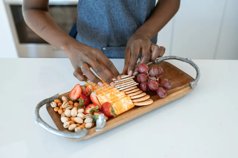 Eine Hand arrangiert bunte Antipasti auf einer rechteckigen Servierplatte für Gäste an einem Tisch.