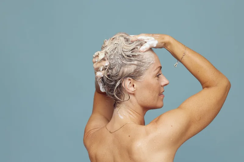 Eine Person wäscht sich die Haare im Badezimmer mit Silbershampoo, um Gelbstich zu neutralisieren.