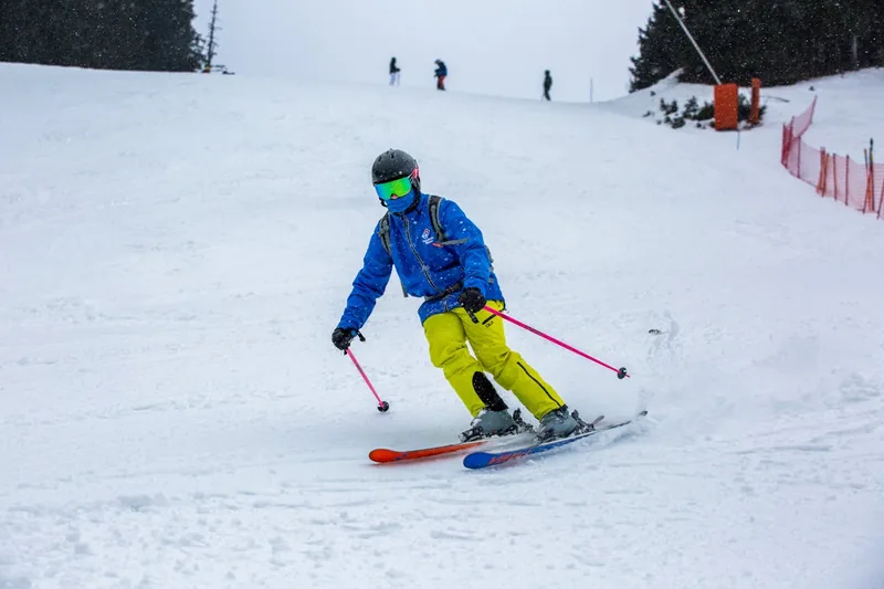 Eine Person mit Skibrille über der Korrektionsbrille beim Skifahren auf einer sonnigen Piste.