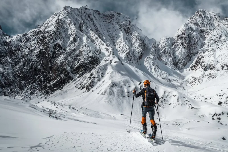 Hände befestigen ein Skifell an einem Tourenski, bereit für den Aufstieg im winterlichen Gelände.