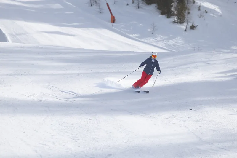 Eine Person in dynamischer Skiposition, die ihre Skihose auf der Piste testet.