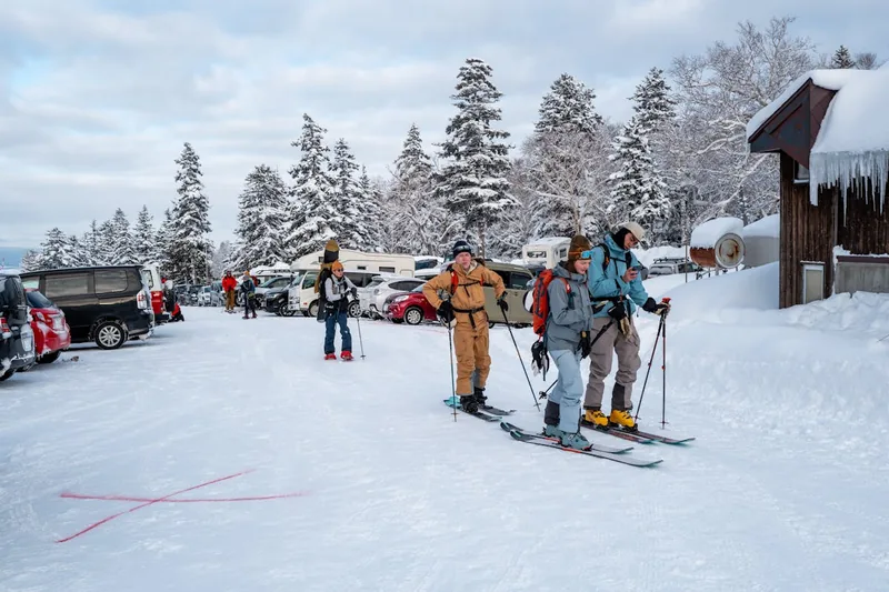 Eine Skitasche und weitere Ausrüstung liegen neben einem Auto auf einem verschneiten Parkplatz im Skigebiet.