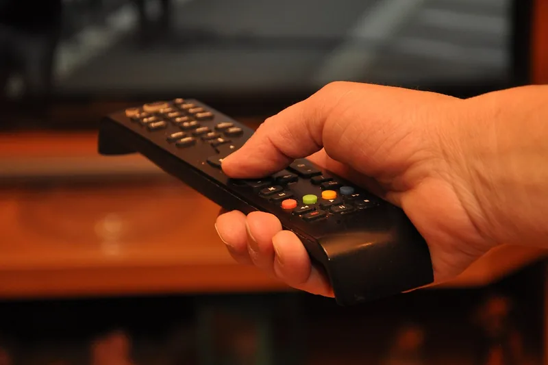 Eine Person bedient einen Smart-TV mit einer Fernbedienung, wählt Streaming-Inhalte aus.