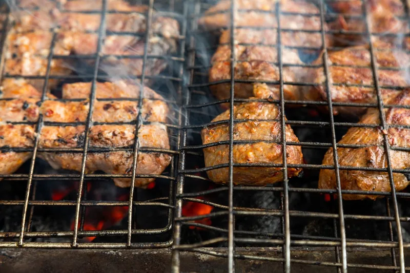 Eine Hand legt zarte Rippchen auf den Rost eines Smoker Grills, Rauch steigt auf.