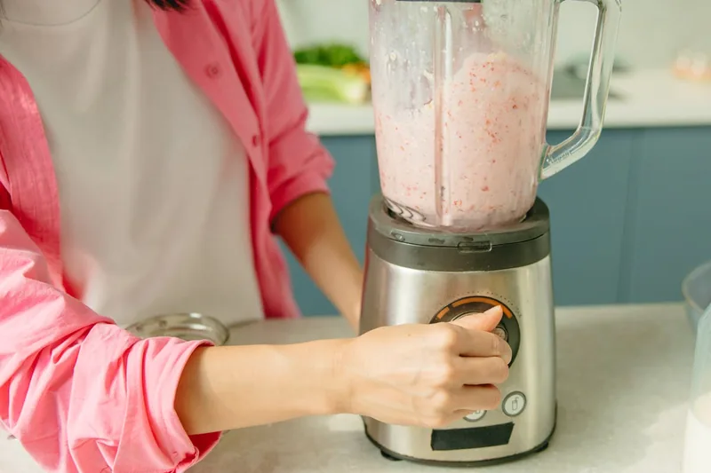 Eine Person bereitet mit einem Smoothie Mixer frische Früchte zu einem gesunden Getränk in der Küche.