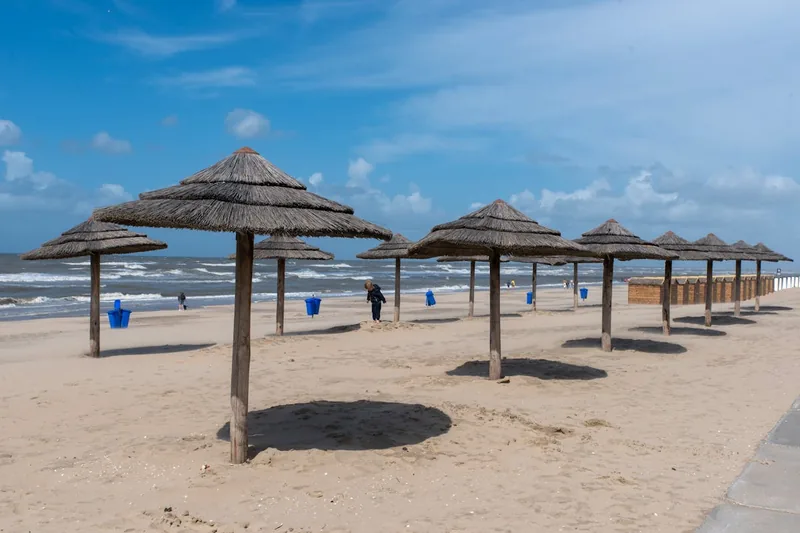 Idyllische Strandszene mit einem stabil im Sand verankerten Sonnenschirm-Erdspieß, der Schatten spendet.