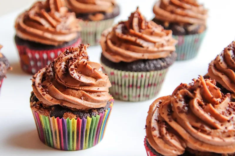 Tisch voller farbenfroh dekorierter Cupcakes und Gebäcke, die mit Spritzbeuteln verziert wurden.