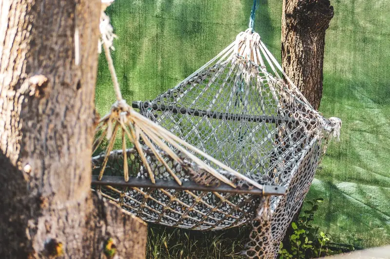 Eine Person entspannt sich genüsslich in einer Stabhängematte im eigenen Garten unter blauem Himmel.