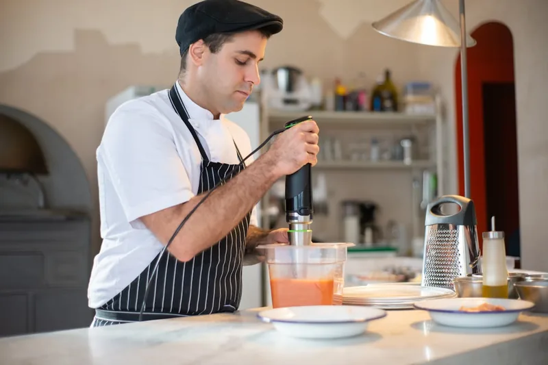 Eine Hand püriert frische Suppe in einem Topf mit einem Stabmixer, aktive Anwendung.