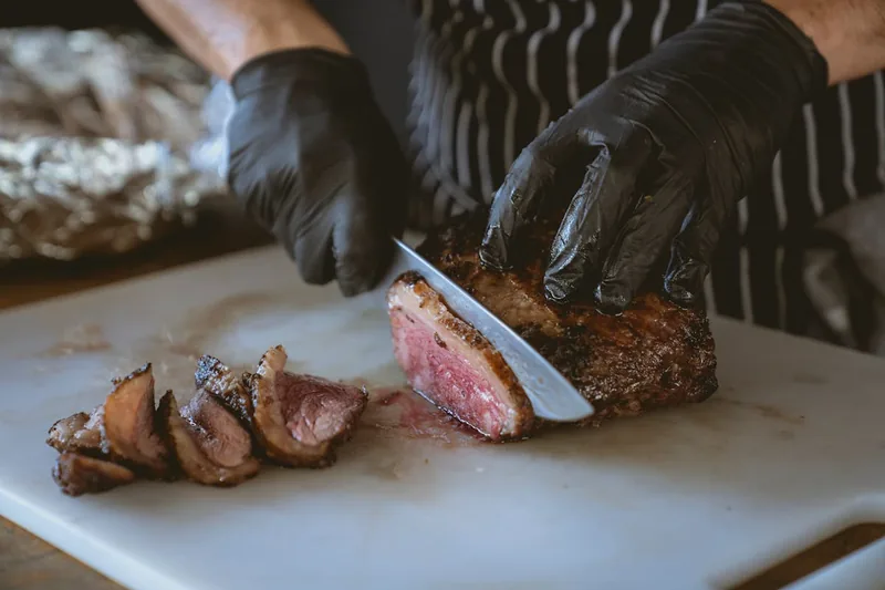 Eine Person schneidet mit einem scharfen Steakmesser ein perfekt gegrilltes Steak auf einem Teller.