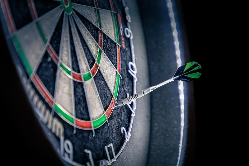 Ein Dartspieler beim konzentrierten Wurf auf eine Steeldartscheibe, zeigt die Spielpraxis.