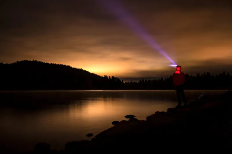 Stimmungsvolle Nachtszene im Wald beim Camping, beleuchtet vom Licht einer LED Stirnlampe.
