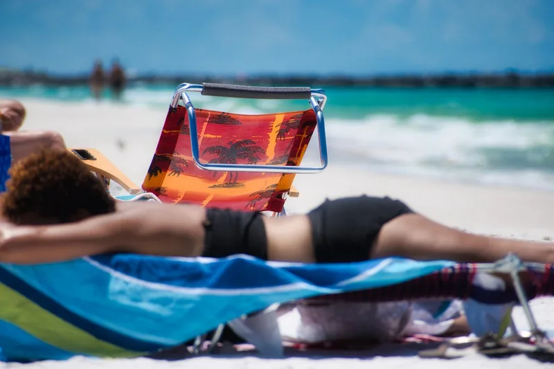 Eine entspannte Person liegt auf einer Strandmatte mit Rückenlehne am Meer, genießt die Sonne.