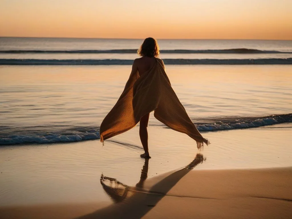 Eine Person mit dem Rücken zur Kamera breitet ein großes, leuchtendes Mikrofaser-Strandtuch auf nassem Sand am Strand aus, mit leichtem Sonnenlicht.