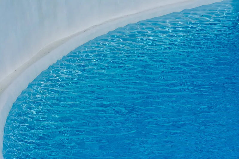 Ein runder Aufstellpool im Garten, klar im Vordergrund, mit blauer Innenfolie für Badespaß.