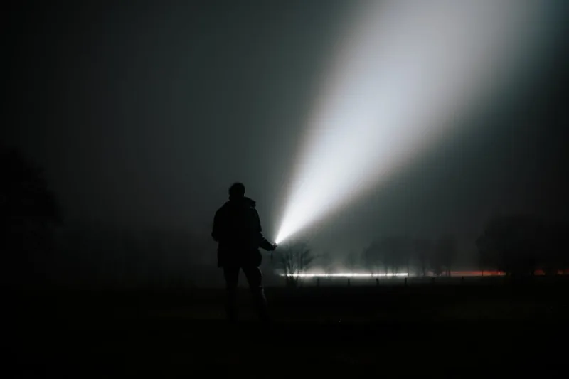 Ein kräftiger Lichtstrahl einer 1000 Lumen Taschenlampe erhellt einen dunklen Waldweg in der Nacht.