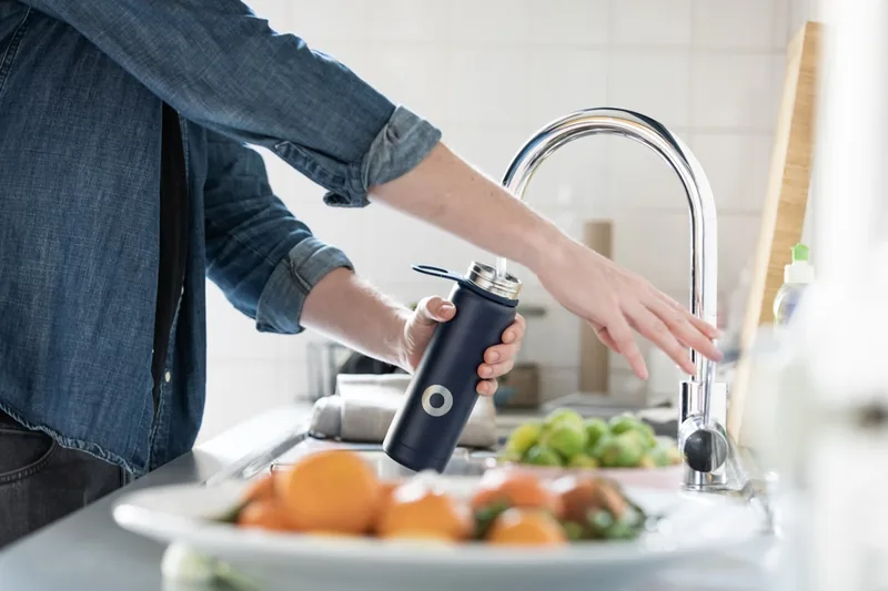 Eine Person reinigt eine Thermoflasche unter fließendem Wasser im Spülbecken in der Küche.