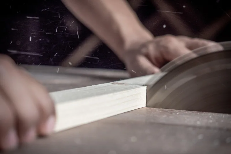 Handwerker bei der Arbeit, präzises Schneiden eines Holzstücks mit einer Tischkreissäge in der Werkstatt.
