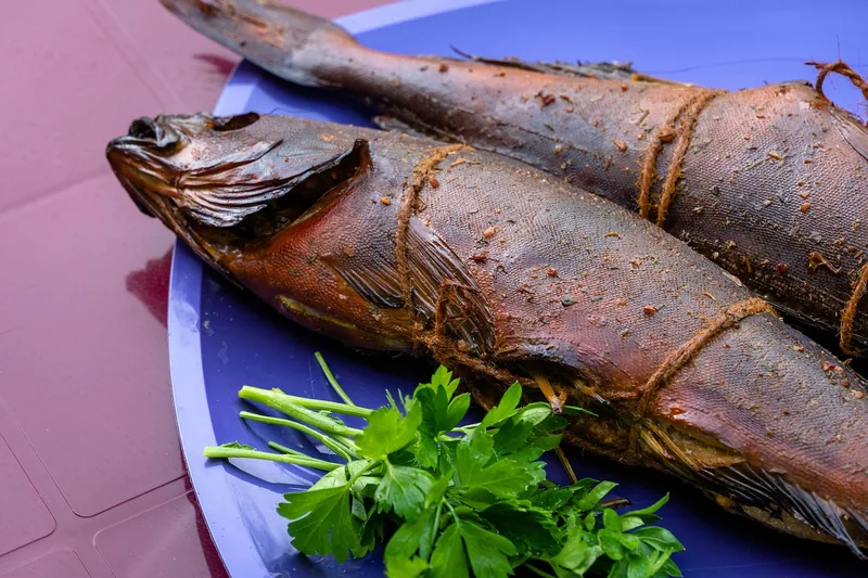 Fertig geräucherter Fisch appetitlich angerichtet auf einem Tisch im Grünen.
