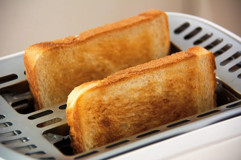 Eine Hand legt Brotscheiben in einen funktionierenden 4-Scheiben Toaster für das Frühstück.
