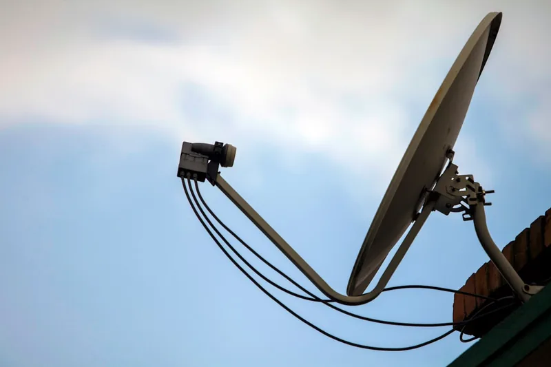 Eine Person installiert vorsichtig ein Twin-LNB am Feed-Arm einer Satellitenschüssel für optimalen Empfang.