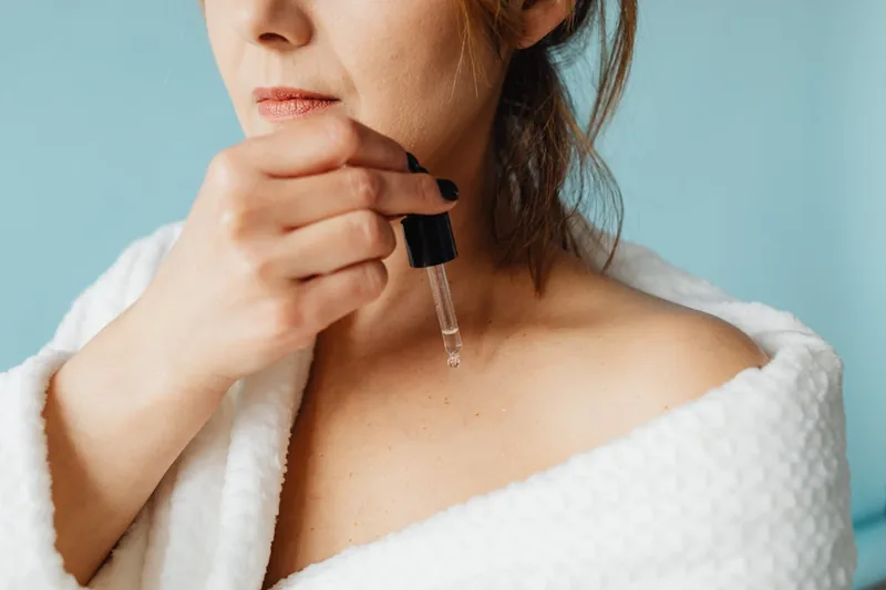 Eine Person trägt sanft Vitamin-C-Serum mit den Fingerspitzen auf ihre Gesichtshaut auf.