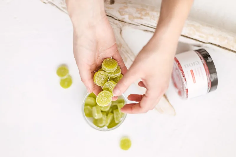 Eine Hand nimmt ein Vitamin-Gummibärchen aus einer Dose, symbolisiert die tägliche Einnahme.
