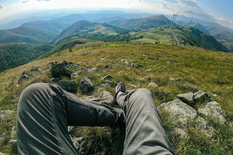 Weitwinkelaufnahme einer Person auf einem Bergpfad, die Aussicht genießt, Symbol für unbeschwertes Wandern.