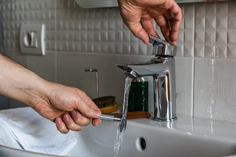 Eine Hand betätigt eine moderne Waschtischarmatur, aus der sanft Wasser in das Waschbecken fließt.
