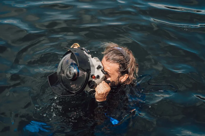 Eine Person beim Schnorcheln, die eine wasserdichte Kamera unter Wasser bedient und Fotos macht.