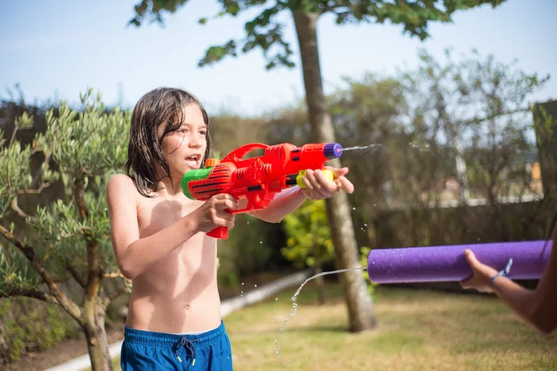 Eine Person im Garten, die eine große Wasserpistole während einer lebhaften Wasserschlacht abfeuert.