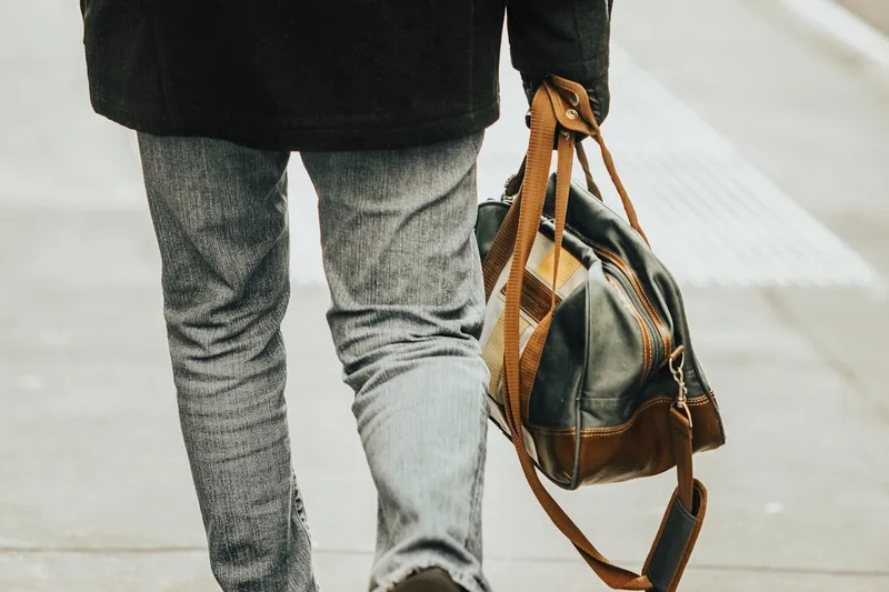 Eine Person trägt einen stilvollen Weekender Reisebeutel lässig über der Schulter am Flughafen.