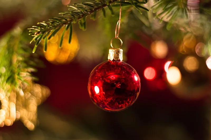 Eine Hand hängt eine personalisierte Weihnachtskugel an einen festlich geschmückten Baum, für eine eigene Note.