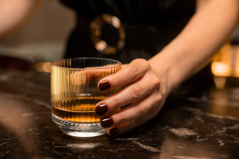 Stimmungsvolle Lounge-Szene mit einem Whiskyglas, Flasche und einem offenen Buch auf einem Tisch.