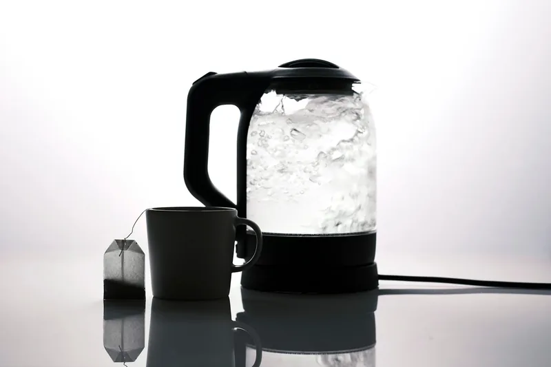 Eine Person gießt präzise heißes Wasser aus einem Wasserkocher in eine Tasse.